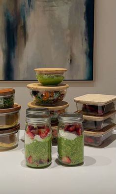 there are many jars with food in them on the table and one has a painting behind it