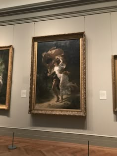 three paintings on display in a museum with wooden floors and white walls, one is holding a dog