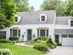 a white brick house with green doors and windows in the front yard is surrounded by lush greenery