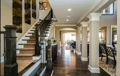 a staircase leading to the upper level of a house with wood floors and white pillars