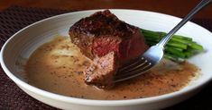 a white bowl filled with meat and gravy next to asparagus