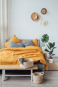 a bed with yellow sheets and pillows in a bedroom next to two plants on the wall