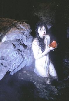 a woman holding a piece of food in her hand while standing next to a rock