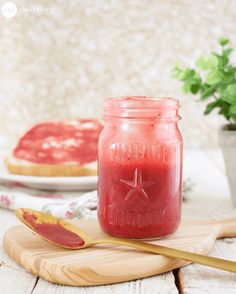 a jar filled with red liquid sitting on top of a wooden table next to a spoon