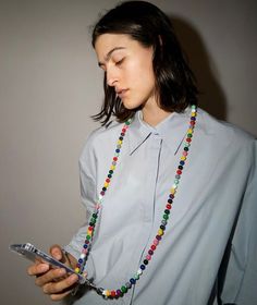 a woman wearing a beaded necklace holding a cell phone and looking at the screen