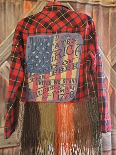 a red, white and blue plaid shirt with fringes on the chest is hanging from a wooden wall