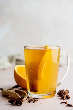 a glass cup filled with tea next to an orange slice and cinnamon sticks on a table