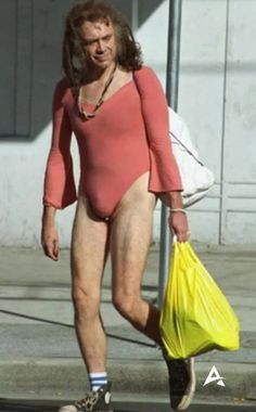 a man in a bodysuit is walking down the street with a yellow shopping bag