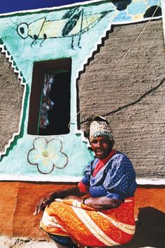 a woman sitting on the ground in front of a building with an artistic design painted on it