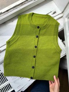 a green sweater vest sitting on top of a window sill next to a woman's hand