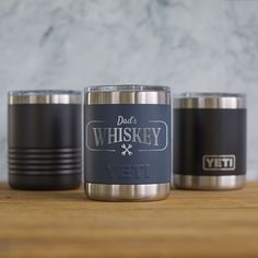 three stainless steel tumblers sitting on top of a wooden table next to each other