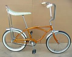 an orange and white bicycle parked in front of a tan wall with black rims