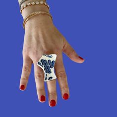 a woman's hand with red nail polish holding a white and blue flower ring