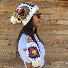 a woman wearing a white hat and crocheted mitt is standing in front of a wooden wall