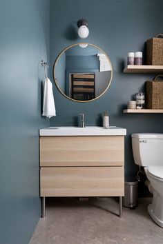 a white toilet sitting next to a bathroom sink under a round mirror on a wall