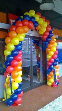 an arch made out of balloons on the side of a building that has glass doors