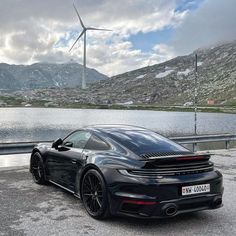 a black sports car parked in front of a lake with wind turbines on the other side