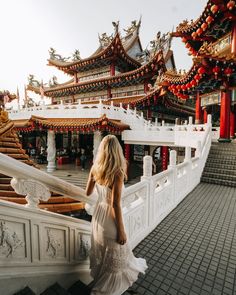 a woman in a white dress is walking down the stairs to a chinese building with red lanterns on it