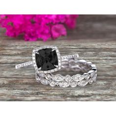 a black and white diamond engagement ring set on top of a wooden table with flowers in the background