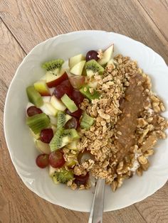 a white plate topped with granola, fruit and nuts