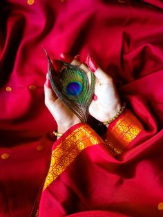 a woman is holding a peacock feather in her hand on a red cloth with gold dots