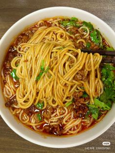 a white bowl filled with noodles and meat on top of a wooden table next to chopsticks