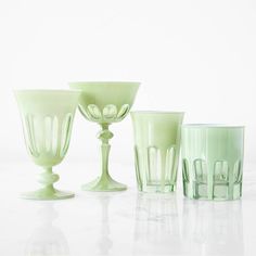 four green glass vases sitting on top of a white table next to each other