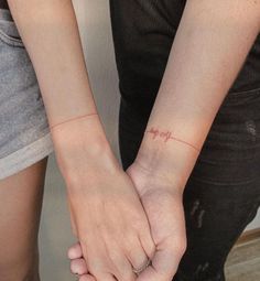 two people holding hands with tattoos on their wrist and the word love written in red ink