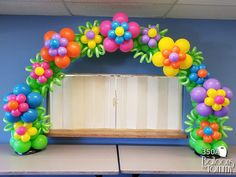 an arch made out of balloons with flowers and leaves on the front is decorated in bright colors