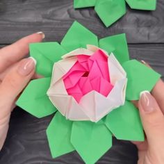 two hands are holding origami flowers with pink and green petals on them,