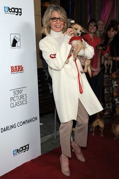 woman in white coat holding small dog on red carpet