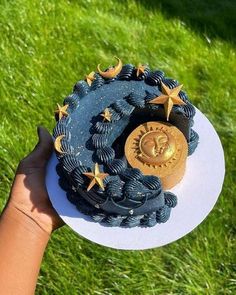 a hand holding a cake with blue icing and gold stars on it in the grass