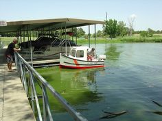 two people standing on a dock next to a boat in the water with fish swimming around