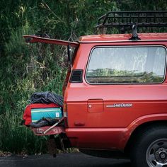 a red truck with luggage in the back parked next to some tall grass and trees