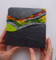 someone is holding up a piece of art made out of slate and colored stones,