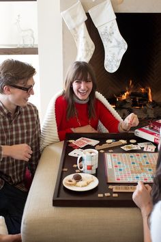 three people sitting at a table playing a board game with stockings hanging above the fireplace