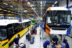 two buses are parked in a factory with workers working on the assembly line next to them