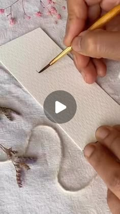 someone is drawing something on paper with a pencil and watercolors in their hands