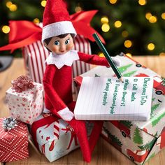 an elf is sitting next to presents and writing on a notepad with a pen