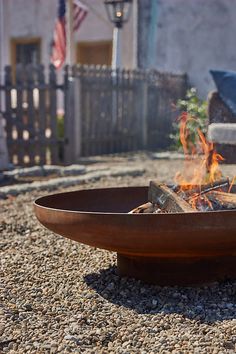 a fire pit sitting on top of gravel next to a fence and american flag in the background