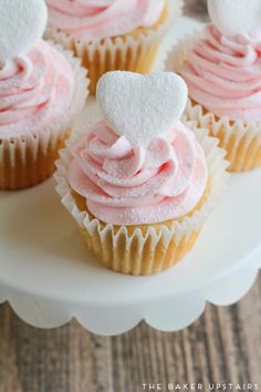 cupcakes with pink frosting and white heart decorations on a cake platter