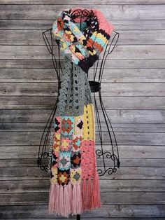 a multicolored crocheted scarf hanging on a mannequin with a wooden wall behind it