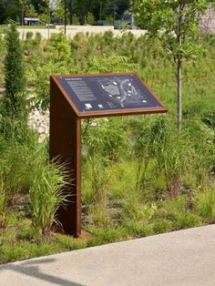 a wooden sign sitting on the side of a road next to a lush green field