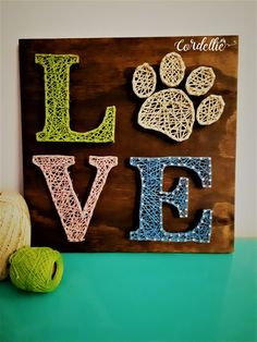 a wooden sign with the word love written in crocheted letters and a ball of yarn next to it