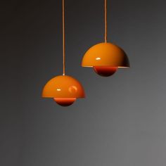 two orange lamps hanging from strings in a room with gray walls and flooring on the wall