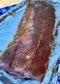 a piece of meat sitting on top of tin foil covered in seasoning next to a knife