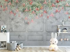 a white rabbit sitting on the floor in front of a wall with pink flowers hanging from it