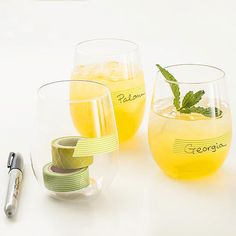 three glasses filled with lemonade and limes next to a silver ball pen on a white surface