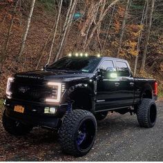 a black truck parked on the side of a road next to some trees and leaves