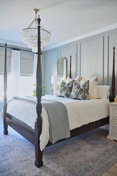 This master bedroom includes a muted blue wall color, a crystal chandelier, a wood bedframe, and blue and white decor items! Primary Bedroom Styling, Blue Guest Bedroom Decor, Rice Beds Bedroom, Blue Bedroom Traditional, Classic Guest Room, Charleston Guest Bedroom, Hampton Cottage Interiors, Blue Vintage Bedroom Ideas, Colonial Bedroom Design